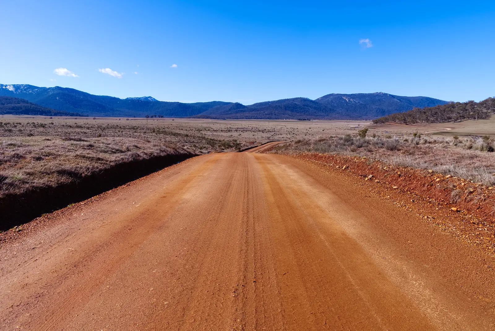 A red dirt road running towards a range of hills under a clear sky