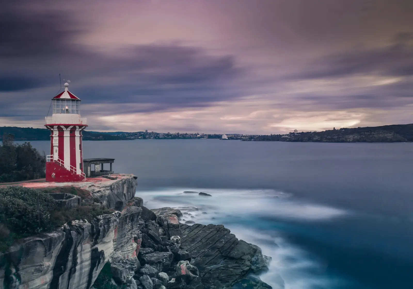 A red and white striped lighthouse on a sandstone headland above the sea at dusk