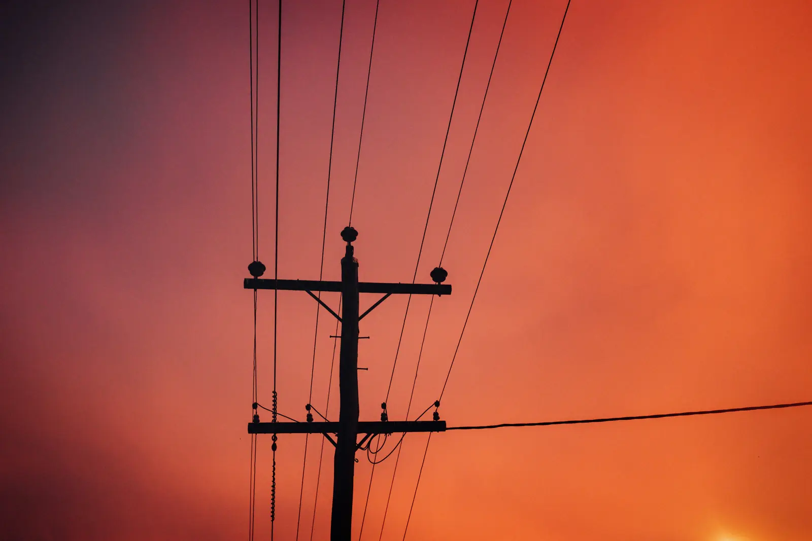 A power pole and lines silhouetted against a red storm sunset in Cairns